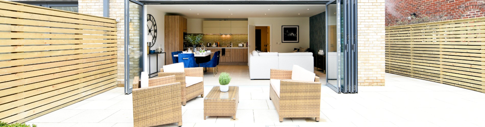 Garden area with stylish wicker furniture and doors folded open fully to reveal kitchen space